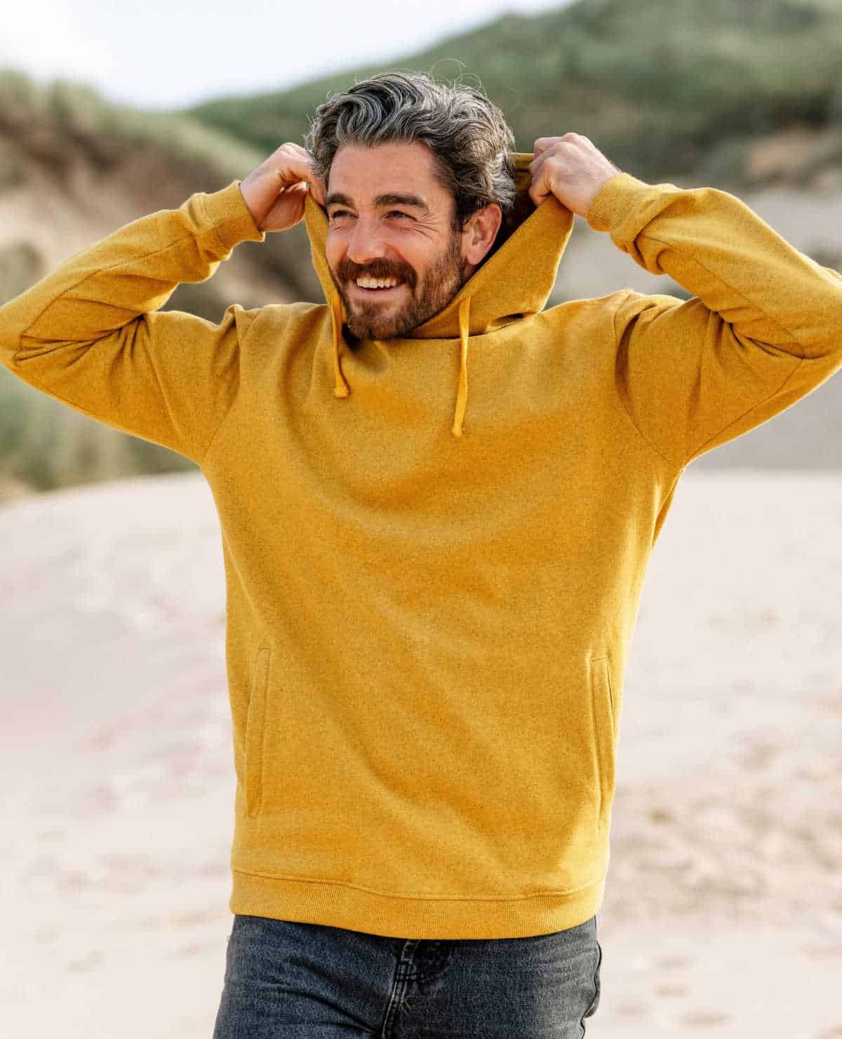 Smiling person on a beach wearing a yellow hoodie from ethical clothing brand Rapanui