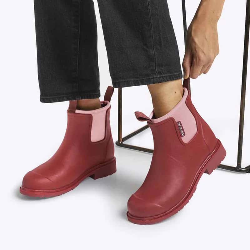 Person in black jeans pulling on a pair of cherry coloured rain boots.