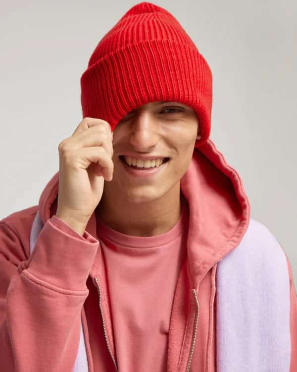 Person wearing a red hat and pink hoodie from sustainable brand Colorful Standard