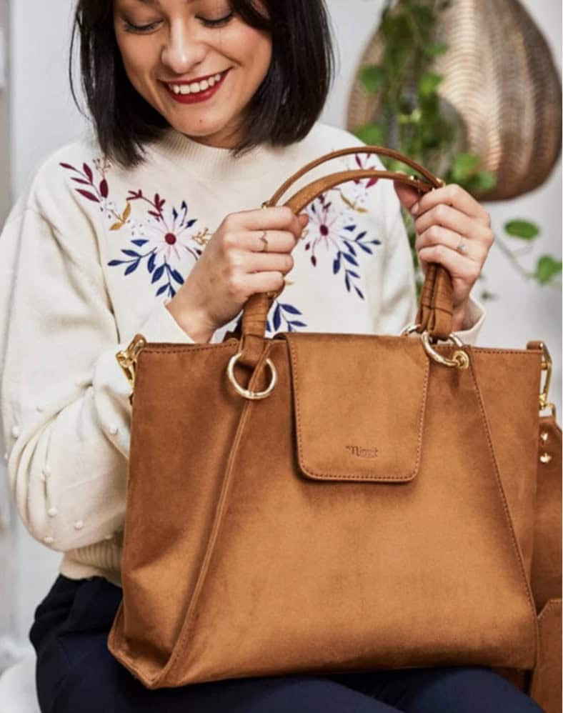 Smiling person in a cream floral jumper holding a brown bag from Immaculate Vegan