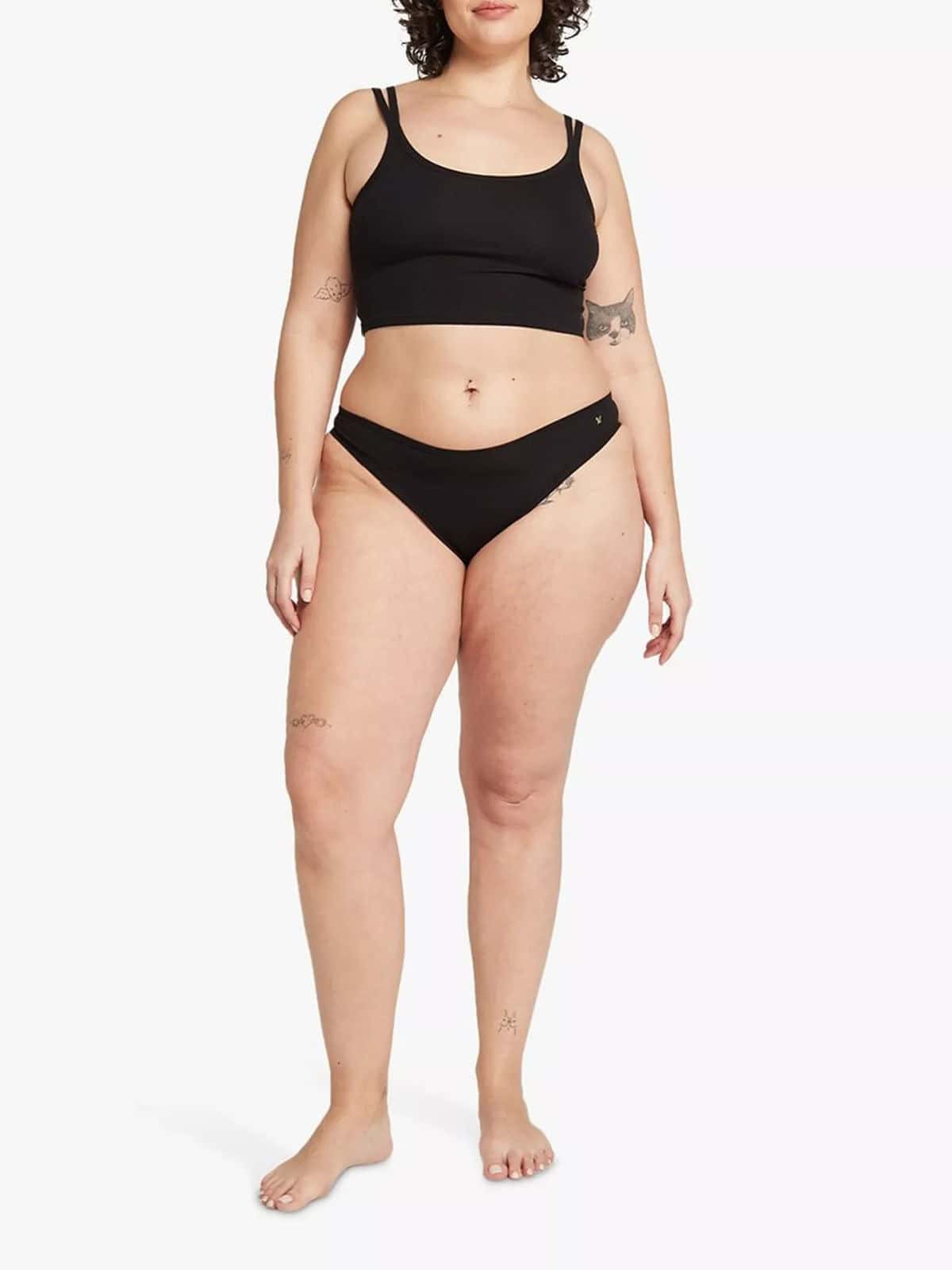 Curly haired person wearing a black bra top and black knickers from Nudea.