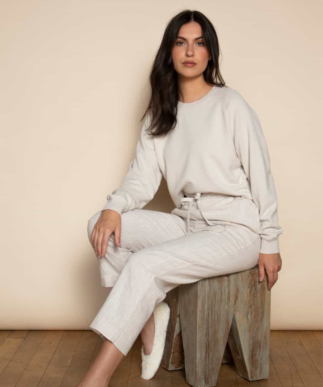 Dark haired person sitting on a stool wearing Dip & Doze trousers and a jumper