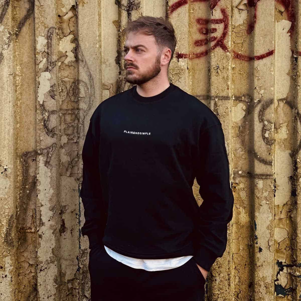 Person wearing a black jumper against a graffiti wall.