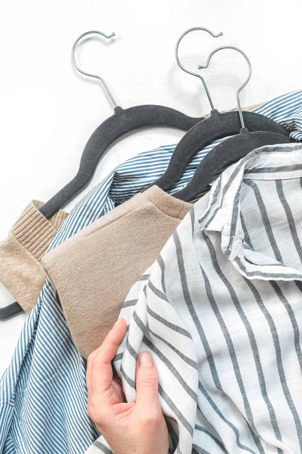 White and blue striped shirt, camel jumper and denim shirt on hangers.