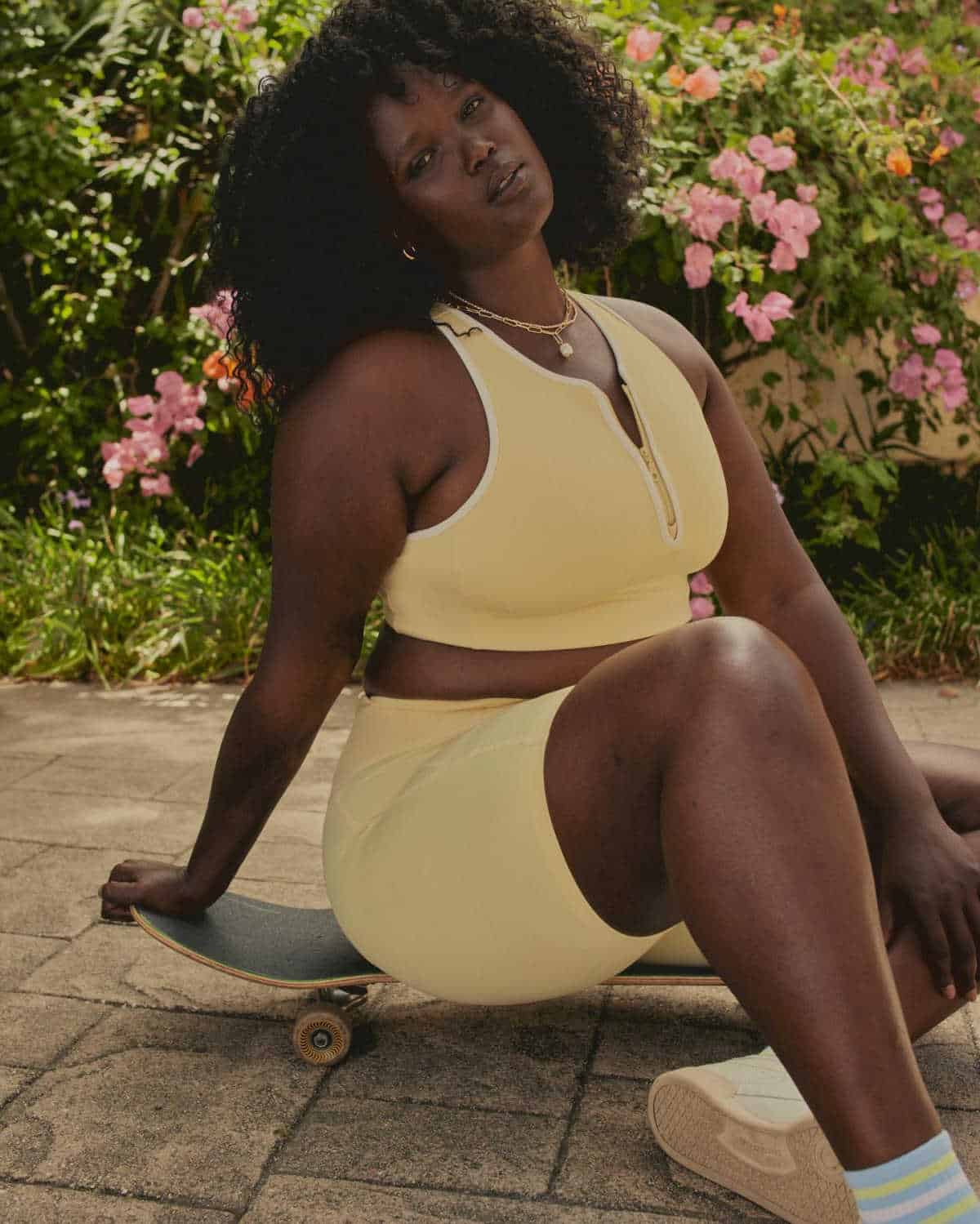 Person sitting on a skateboard wearing a yellow top and shorts from sustainable brand Girlfriend Collective