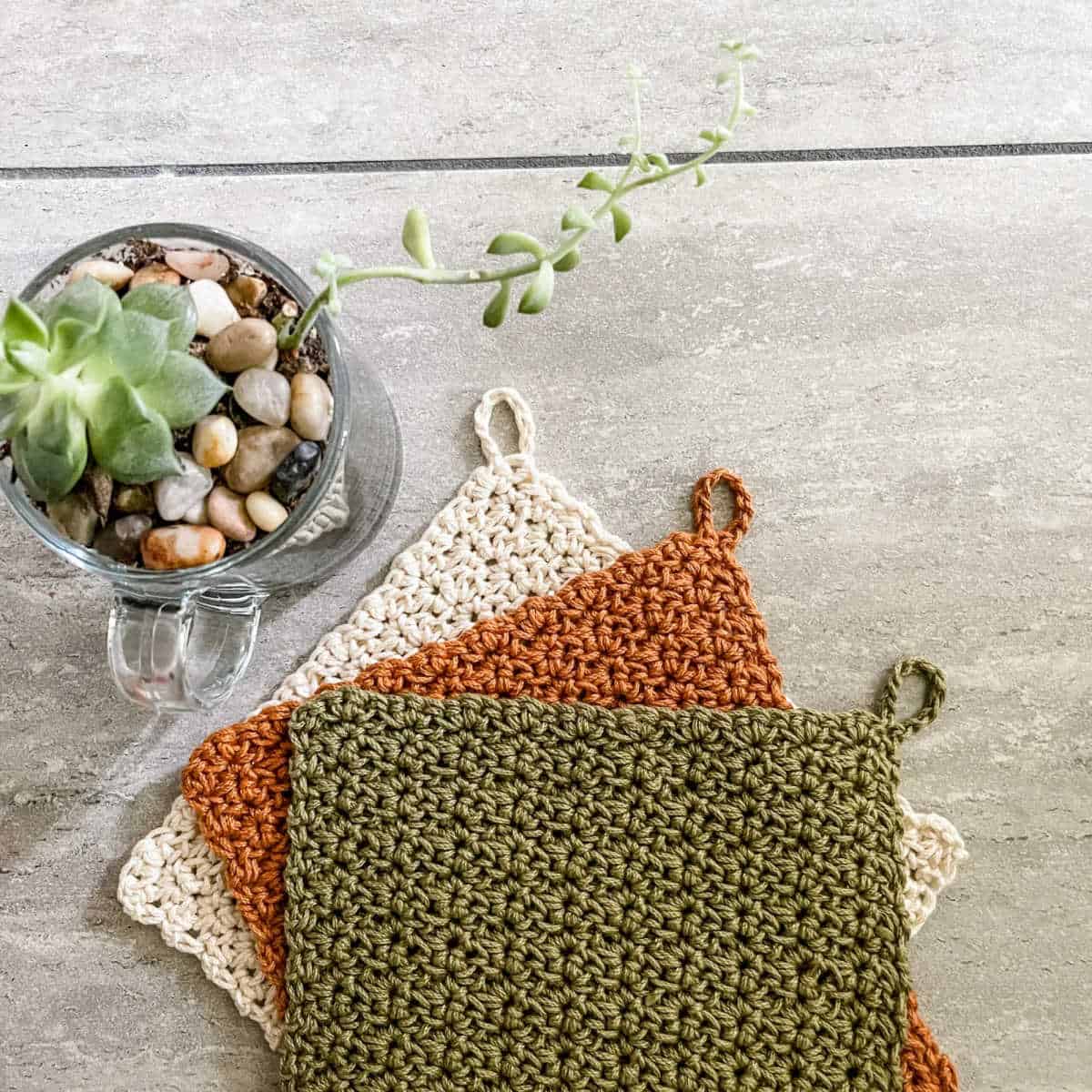 Three crocheted dish cloths in green, rust and cream.