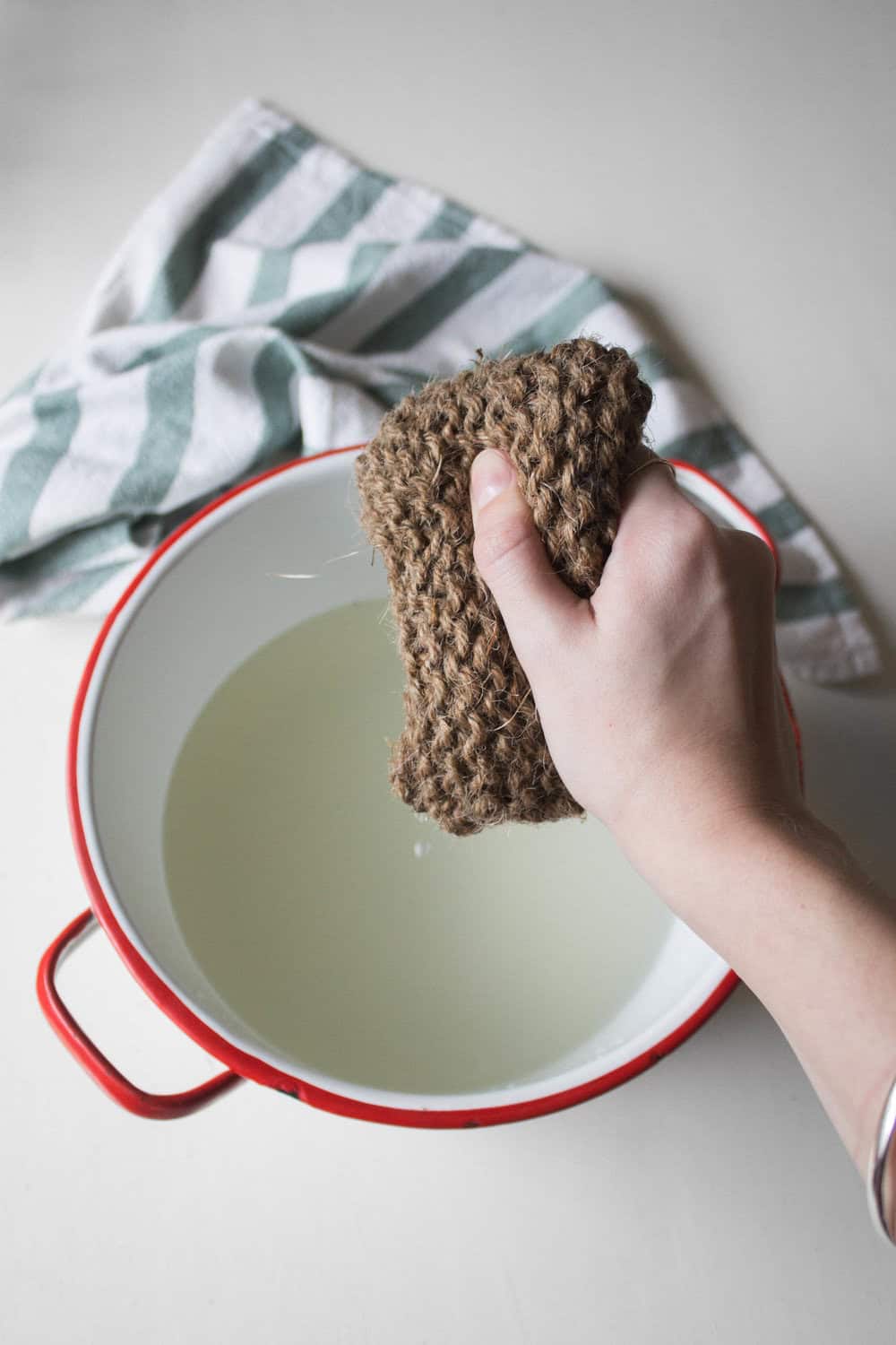 Person holding a zero-waste scouring pad made from twine, next to a pot filled with water.