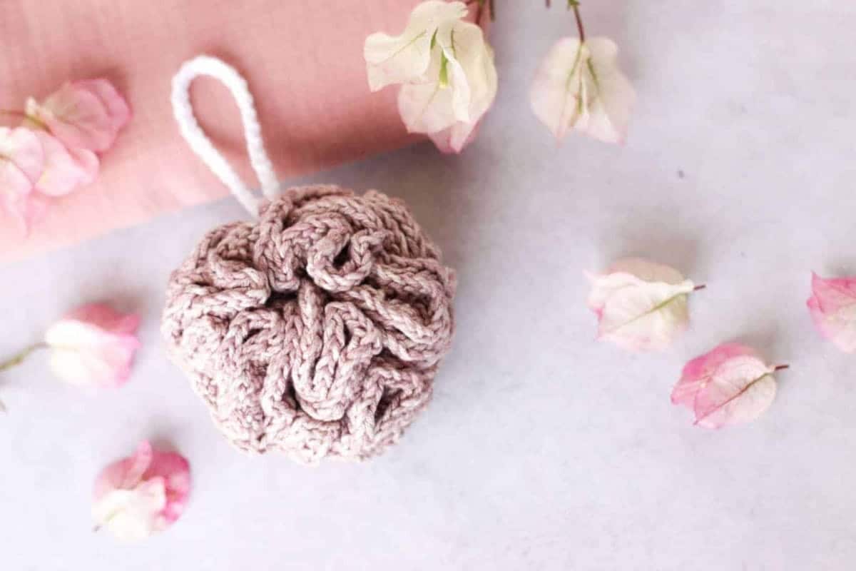 Zero-waste and plastic-free crochet shower pouf in pink with a white hanger.