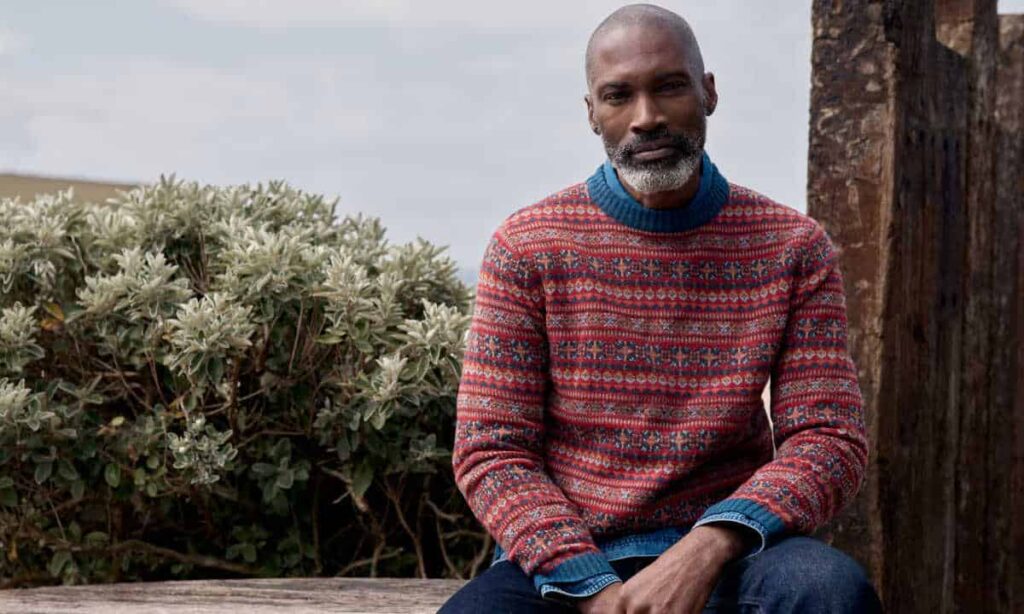 Person wearing a fair isle jumper and denim shirt sitting next to a tree