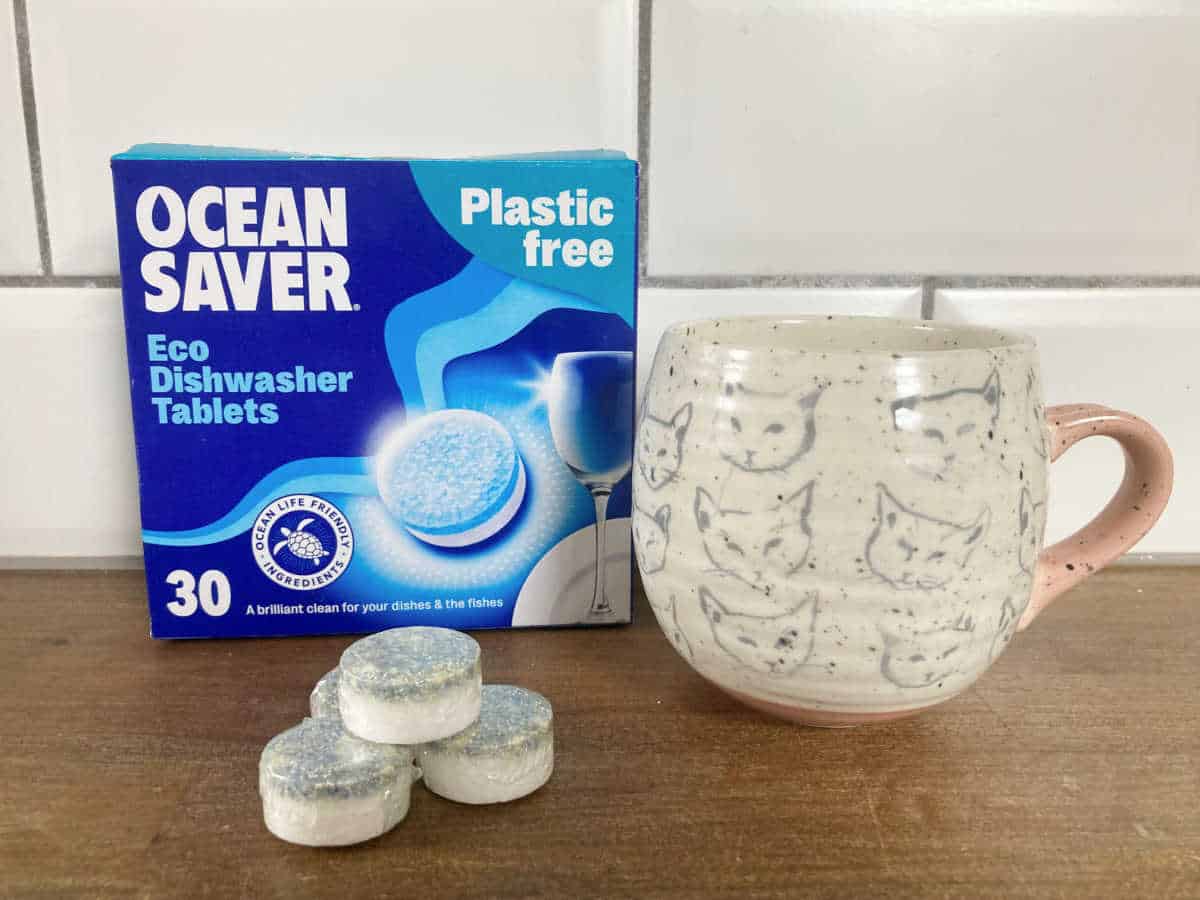 Box of Oceansaver eco dishwasher tablets next to a mug with cats on it, and a pile of dishwasher tabs.