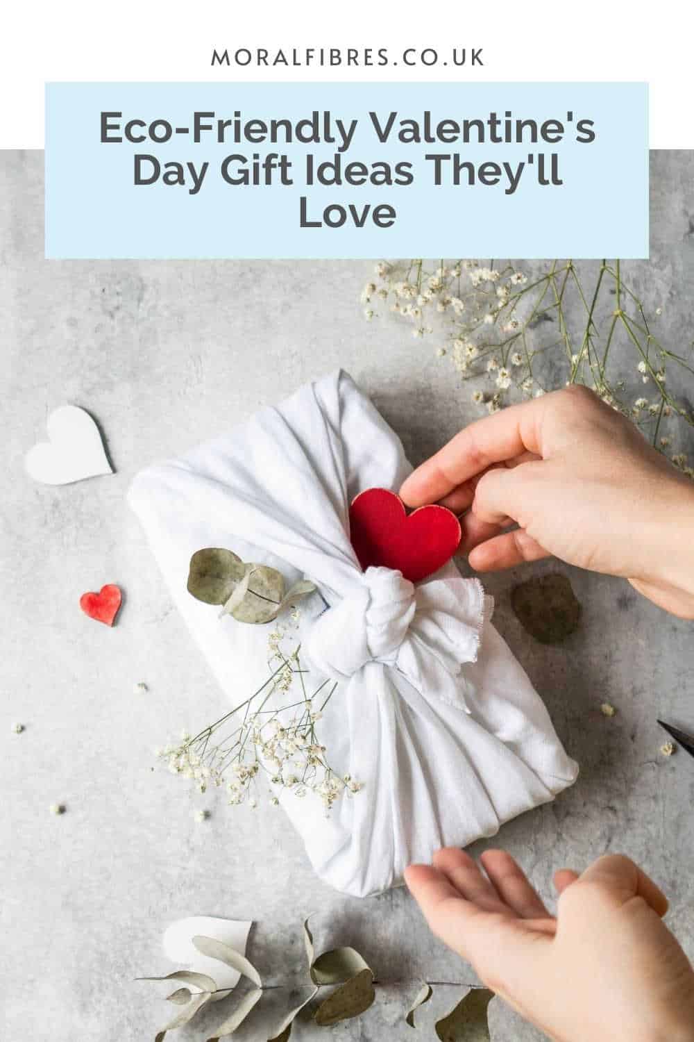 A gift wrapped in white fabric with sprigs of eucalyptus and gypsophila, and a red paper heart, and a blue text box that reads eco-friendly valentine's day gift ideas they'll love.